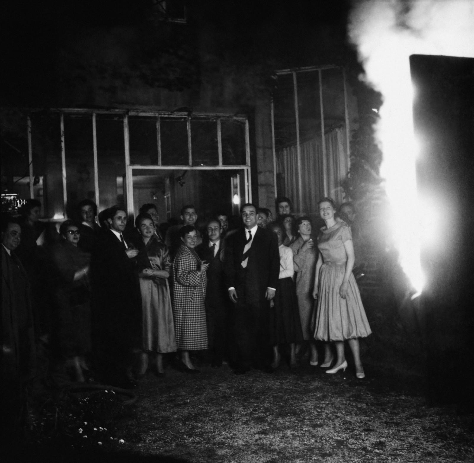 Public devant l'œuvre "Tableau de feu bleu d’une minute", (M 41), avec les feux de Bengale allumés, dans les jardins de la galerie Colette Allendy, Paris, 1957