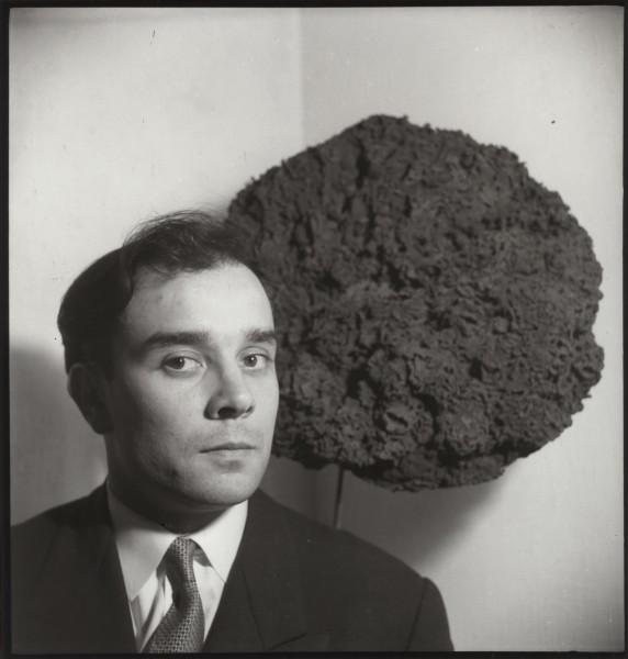 Yves Klein in front of his Sponge Sculpture at the exhibition "Monochrome Propositions of Yves Klein" Gallery One, London